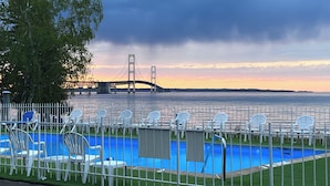 A pool area with white chairs and a view of a bridge in the background. - Riviera Motel (Mackinaw City)