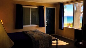 A bedroom with a bed, a door, and a window with a view of the sea. - Riviera Motel (Mackinaw City)