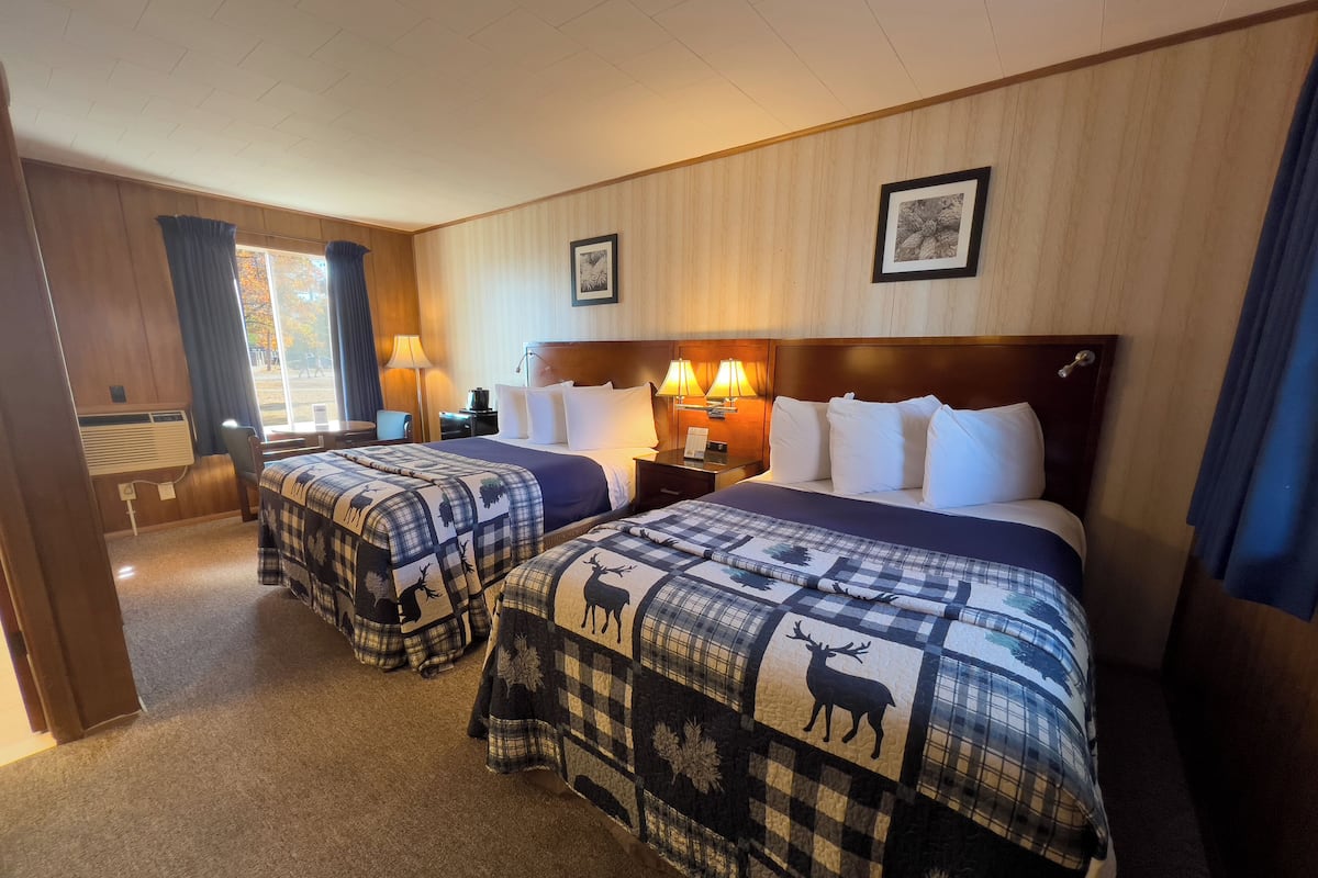 A hotel room with two beds, each with a plaid deer-themed bedspread, a wooden headboard, and a window with curtains.