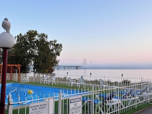 Un espace piscine entouré d’une clôture, avec des chaises et un panneau indiquant qu’il n’y a pas de sauveteur en service.