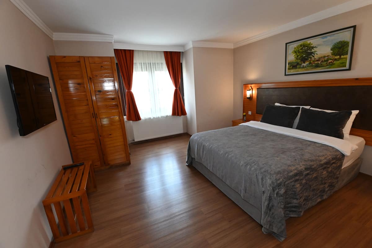 A bedroom with a bed, wooden wardrobe, and a painting on the wall.