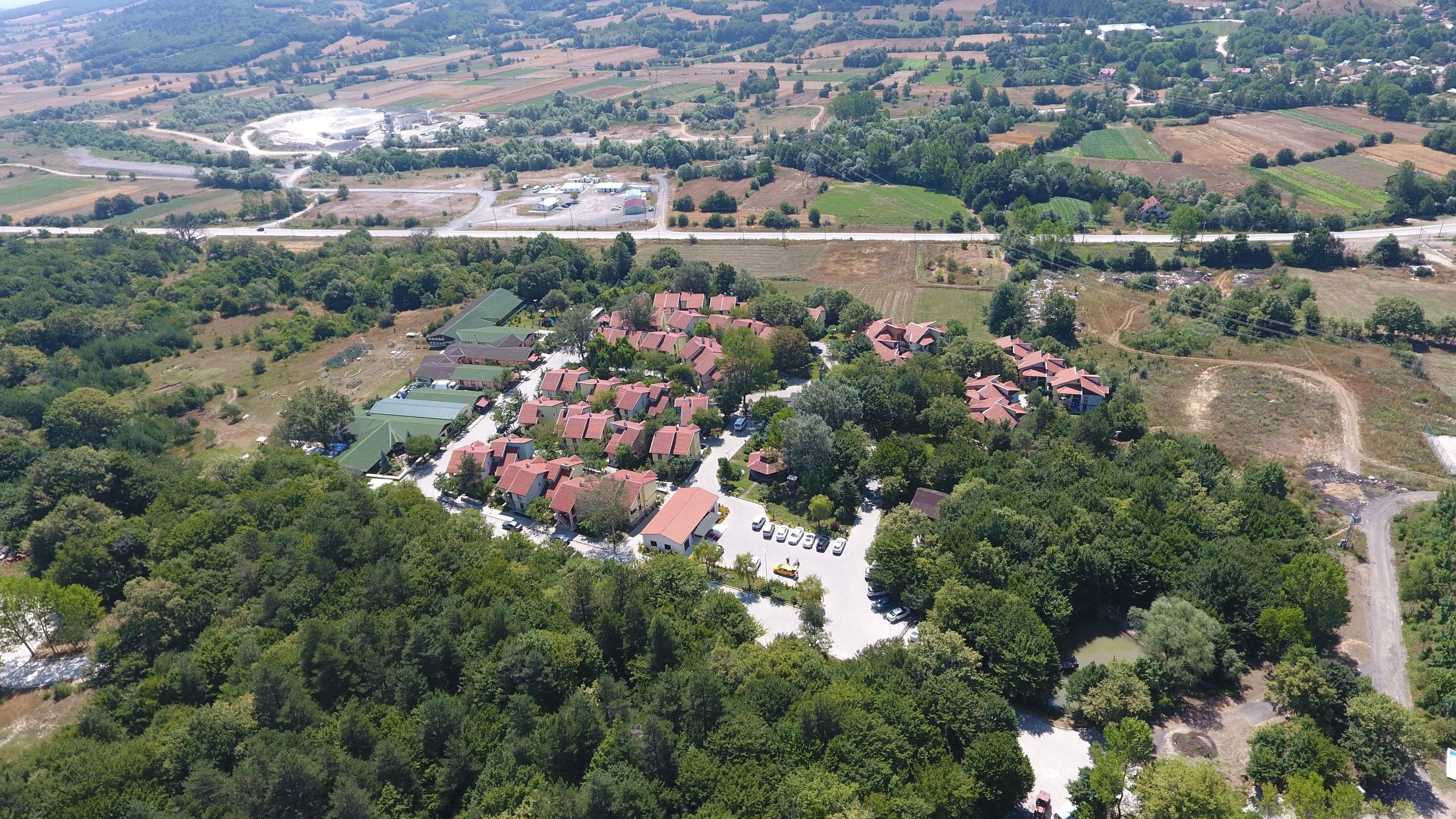 An aerial view of a residential area with multiple houses, a parking lot, and surrounding greenery.
