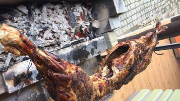 Um frango assado grande, espetado sobre uma fogueira aberta.