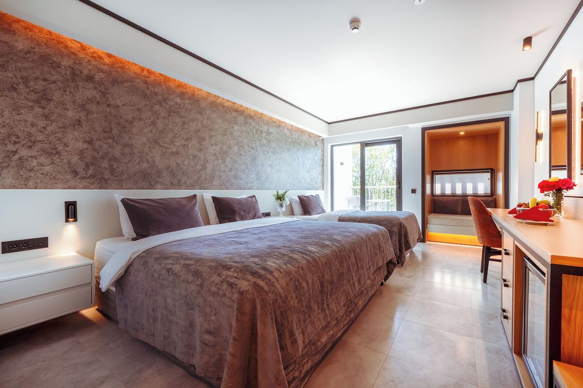 A modern bedroom with a large bed, bedside tables, a desk, and a bathroom visible through an open door.