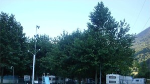 A swimming pool with a slide, surrounded by trees and RVs in a campground setting. - Camping Prado Verde (Vilamos)