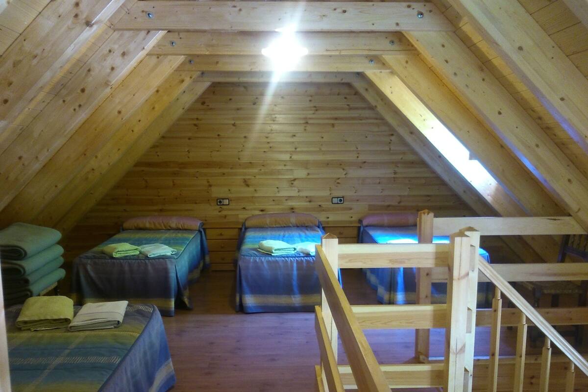 Un dormitorio acogedor en el ático con tres literas, vigas de madera y techo inclinado.