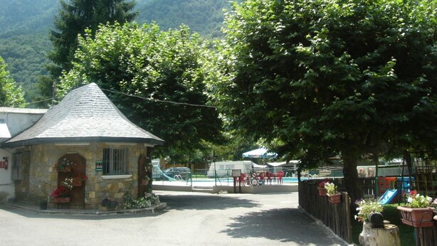 A small stone building with a conical roof, surrounded by lush greenery and mountains in the background. - Camping Prado Verde (Vilamos)