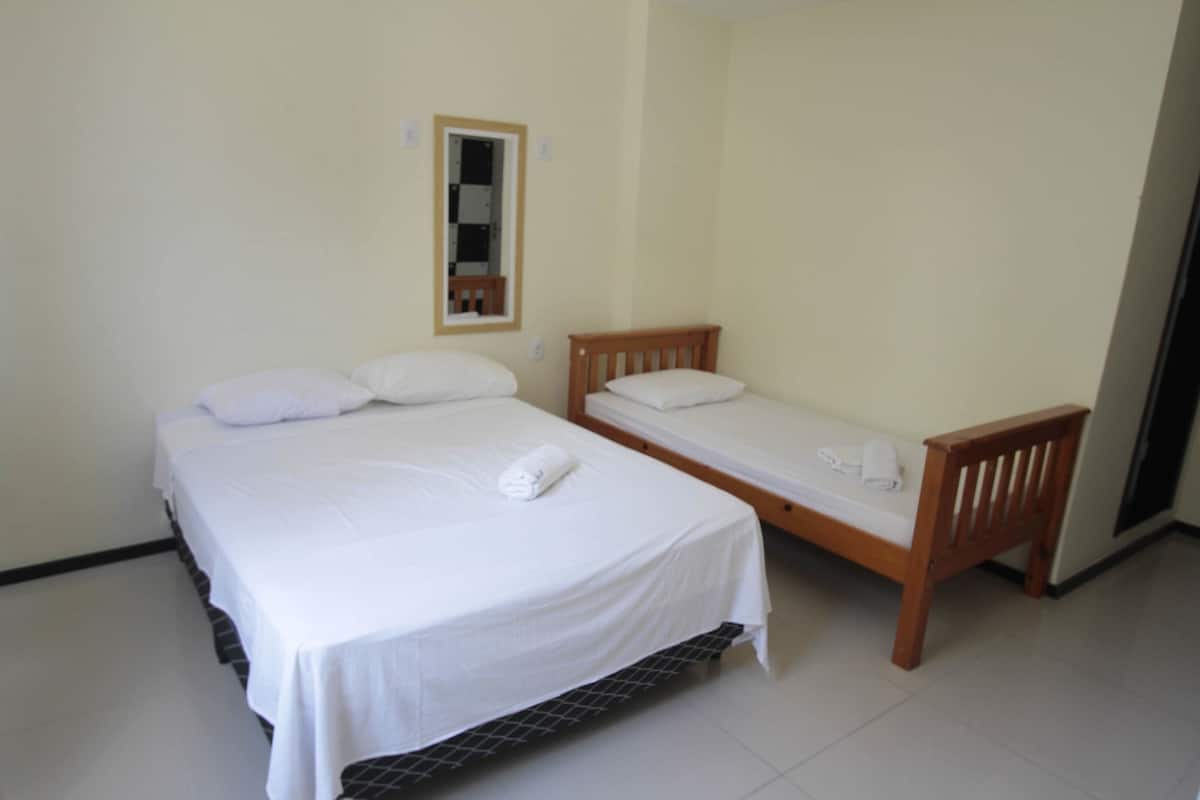 A room with two beds, one larger and one smaller, both with white bedding and pillows.