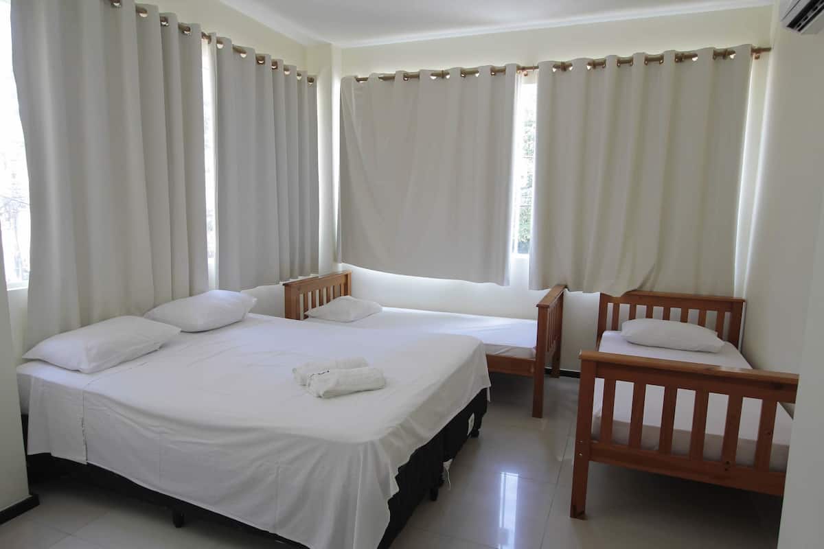 A bedroom with two beds, a wooden chair, and a window with curtains.
