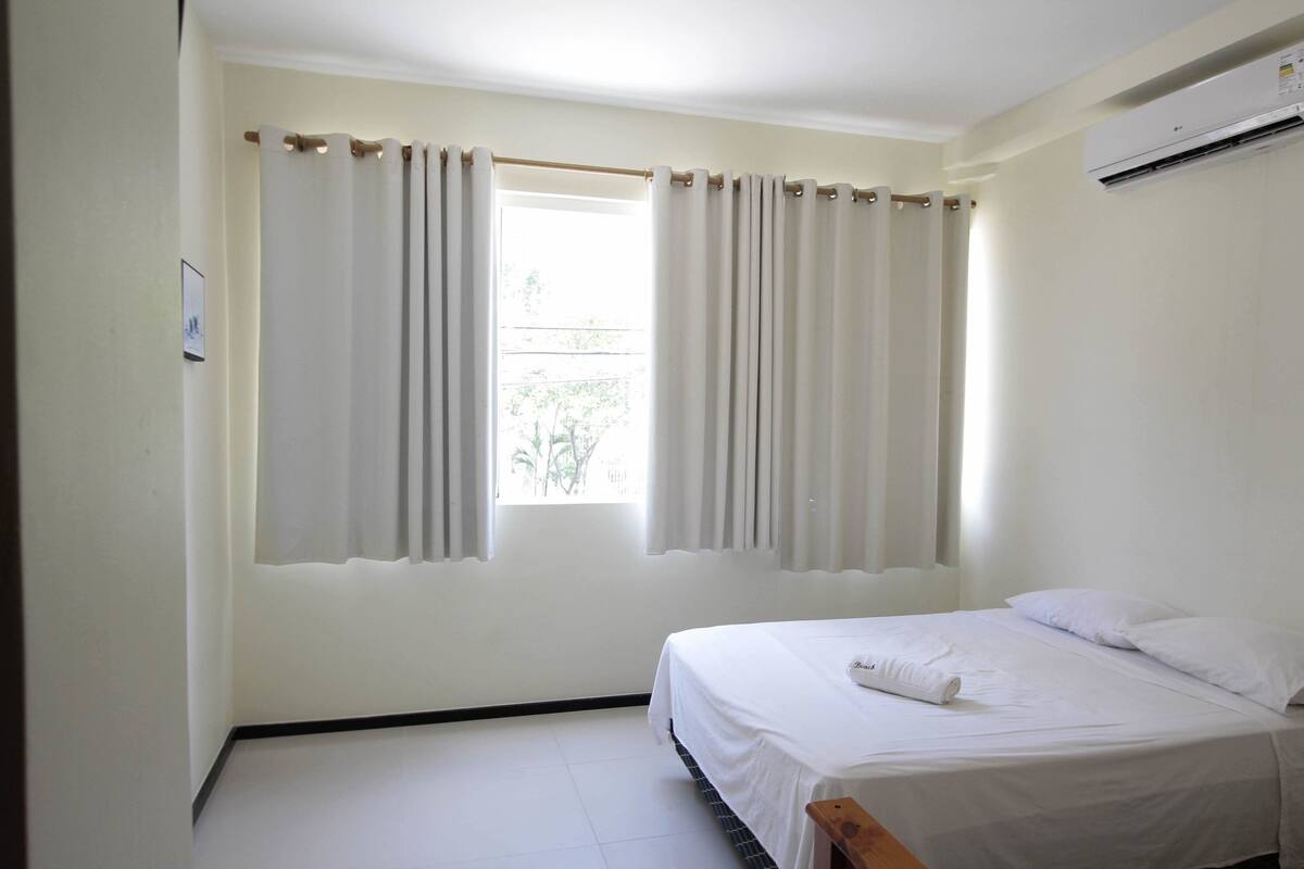 A bedroom with a single bed, white curtains, and an air conditioning unit on the wall.