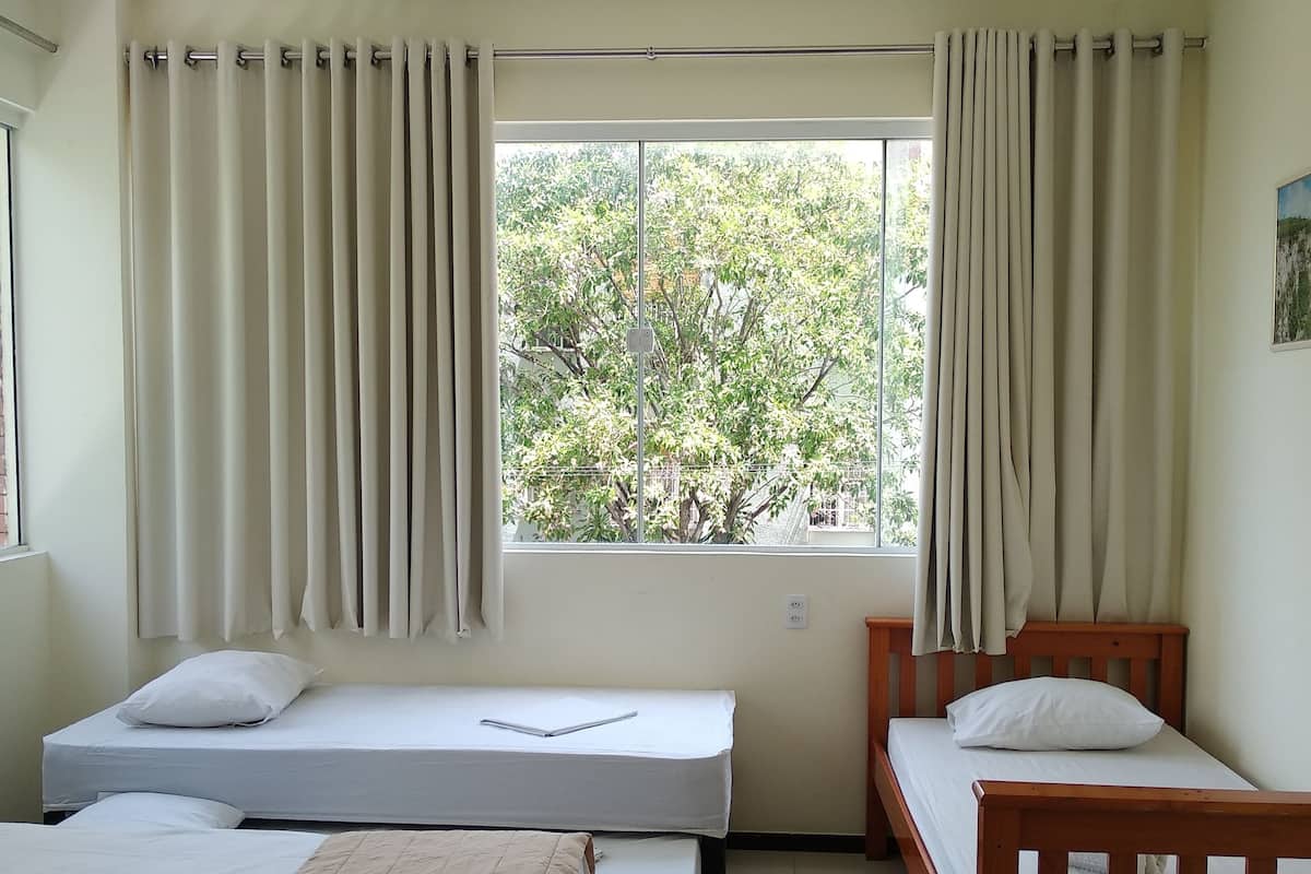 A room with two single beds, a window with curtains, and a ceiling light.