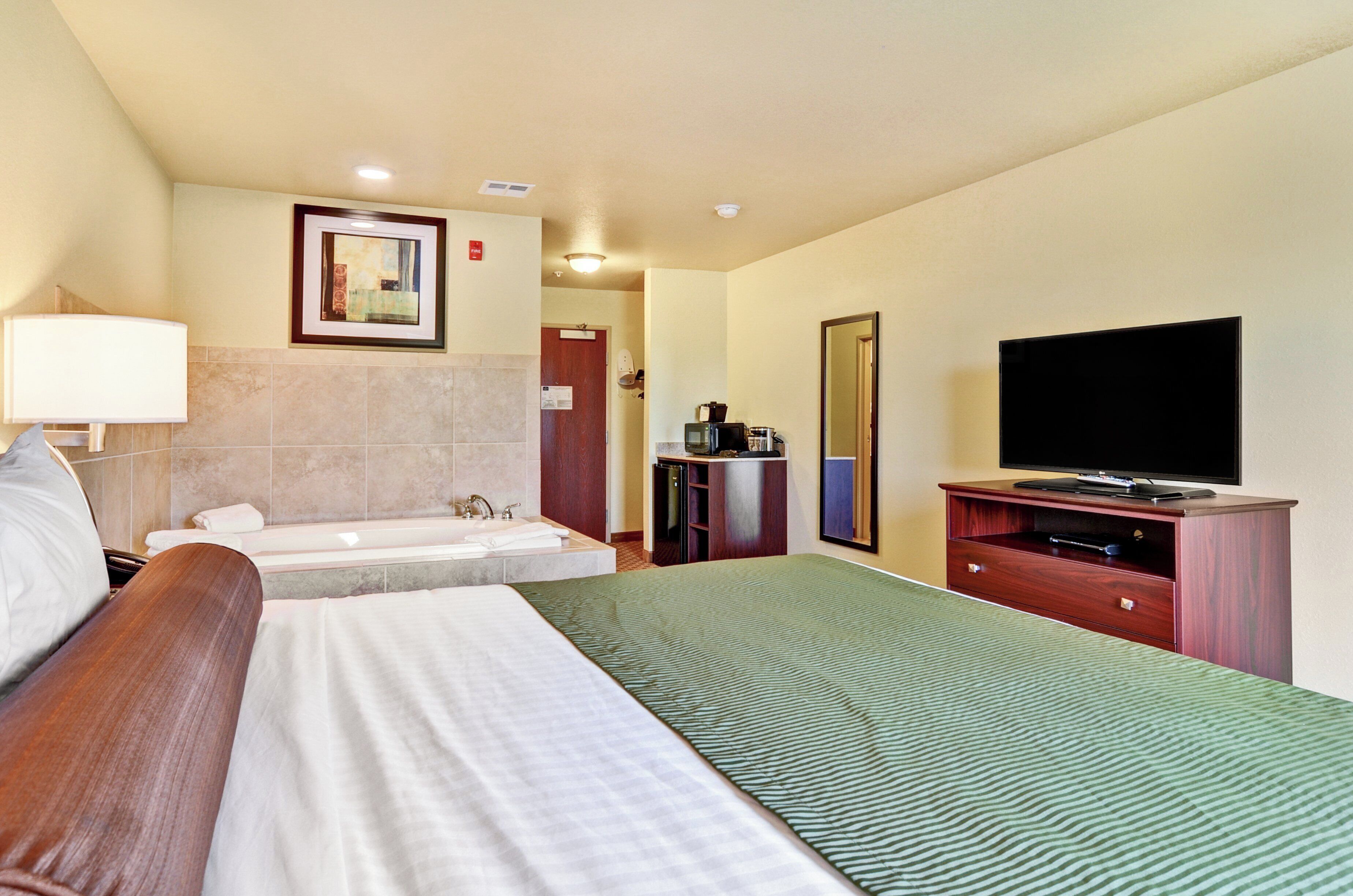 Een hotelkamer met een groot bed, een televisie, een badkamer met bad en een magnetron.