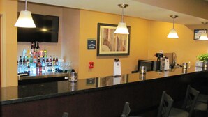 Zona de bar con mostrador, varias botellas, vasos y un televisor montado en la pared.