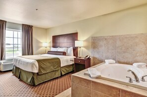 Habitación de hotel con cama, mesita de noche con lámpara, baño con bañera y ventana con cortinas.