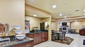 Una cocina de hotel con zona de bufé, comedor con chimenea y televisor montado en la pared.