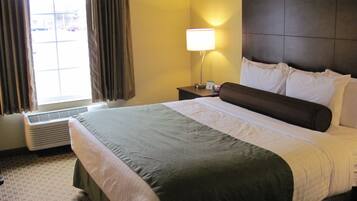Una habitación de hotel con una cama grande, una mesita de noche con una lámpara y una ventana con cortinas.