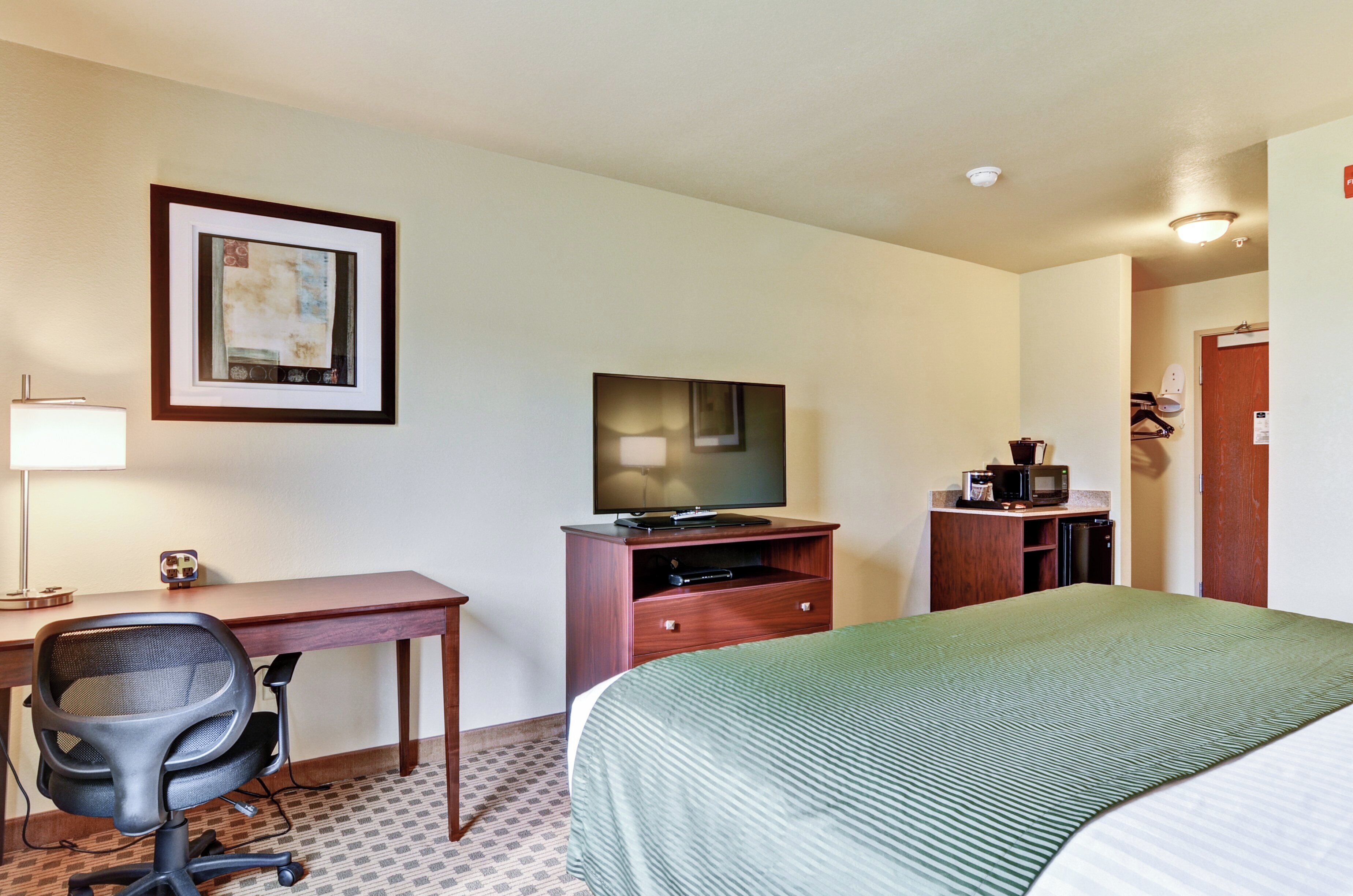 A hotel room with a bed, a desk with a chair, a television, a microwave, and a small cabinet.