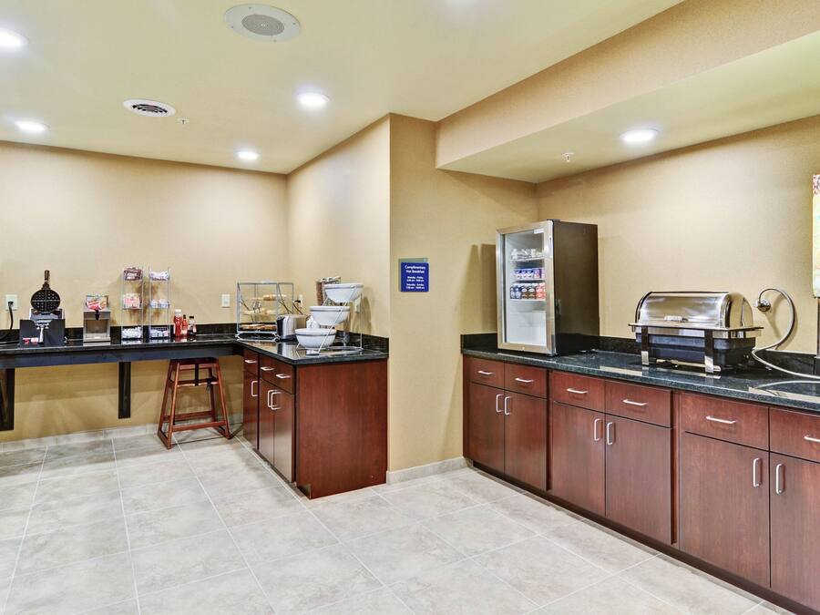 Cocina de hotel con estación de café, refrigerador y un letrero que indica desayuno de cortesía.