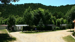A gravel driveway leading to a row of single-story houses with a forested hill in the background.