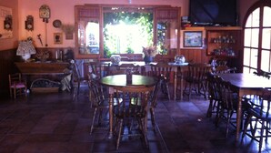 A cozy restaurant with wooden furniture, a large window with greenery, and a TV mounted on the wall.