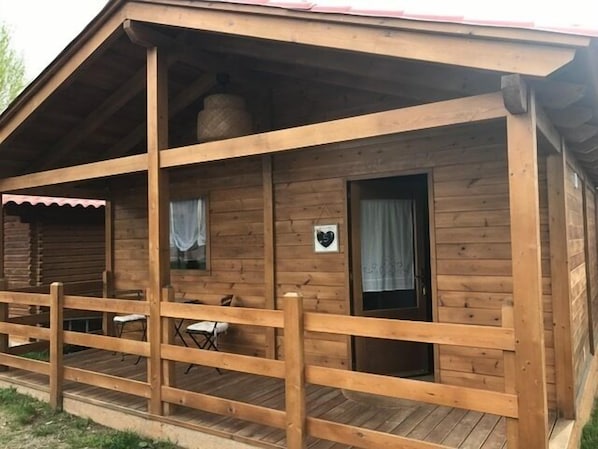 A wooden cabin with a porch, a small table, and a chair.