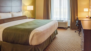 Ein Hotelzimmer mit einem großen Bett, einem Schreibtisch, einem Sessel, einer Lampe und einer Klimaanlage.