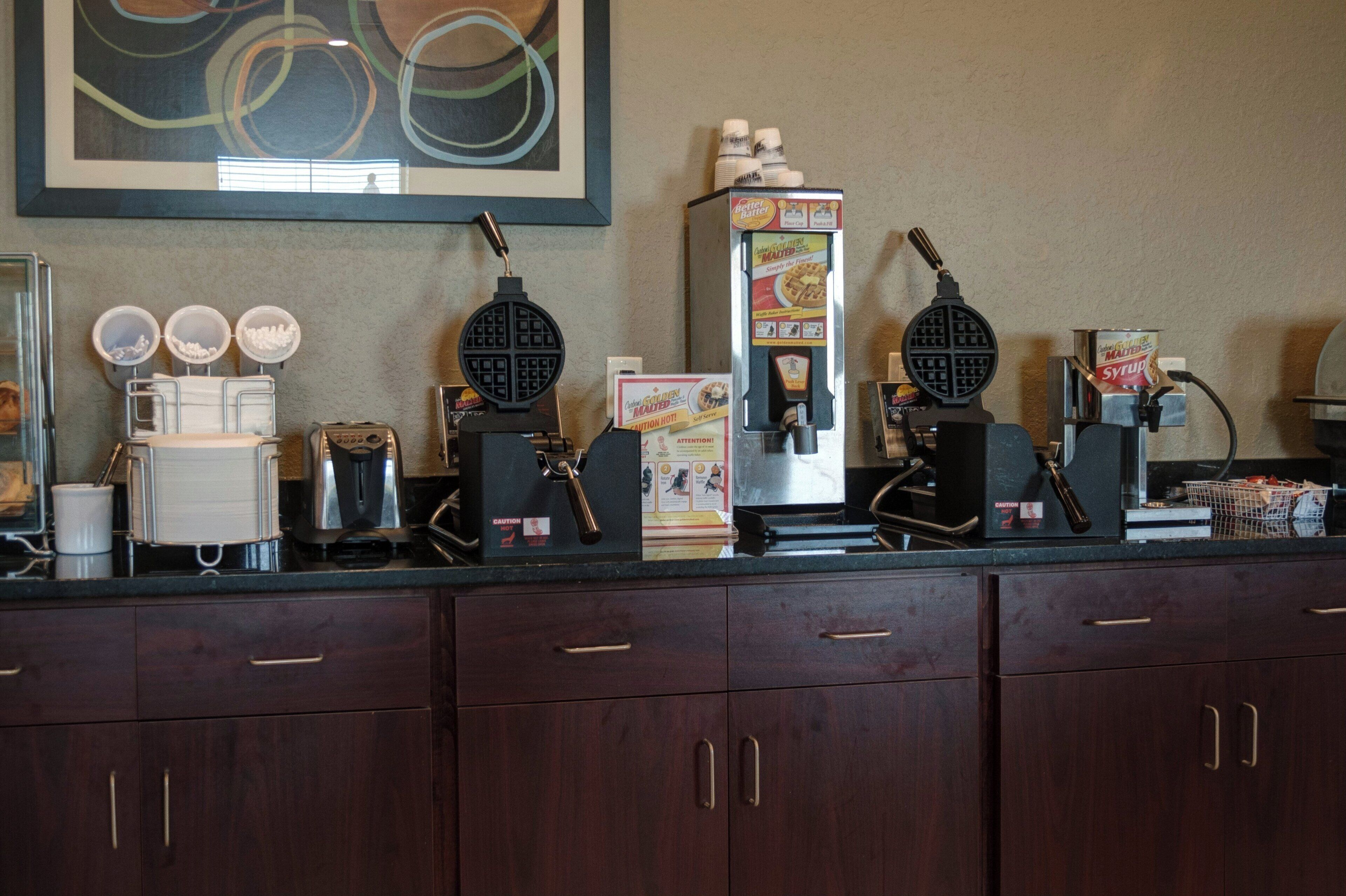 A kitchen counter with waffle makers, a coffee machine, and a syrup dispenser.