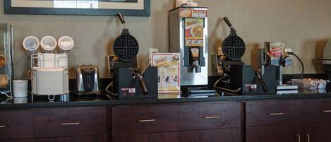 A kitchen counter with waffle makers, a coffee machine, and a syrup dispenser.