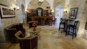 Un área de bar con paredes de piedra, piso a cuadros y taburetes de bar. Hay sillas y una mesa con un jarrón de flores.
