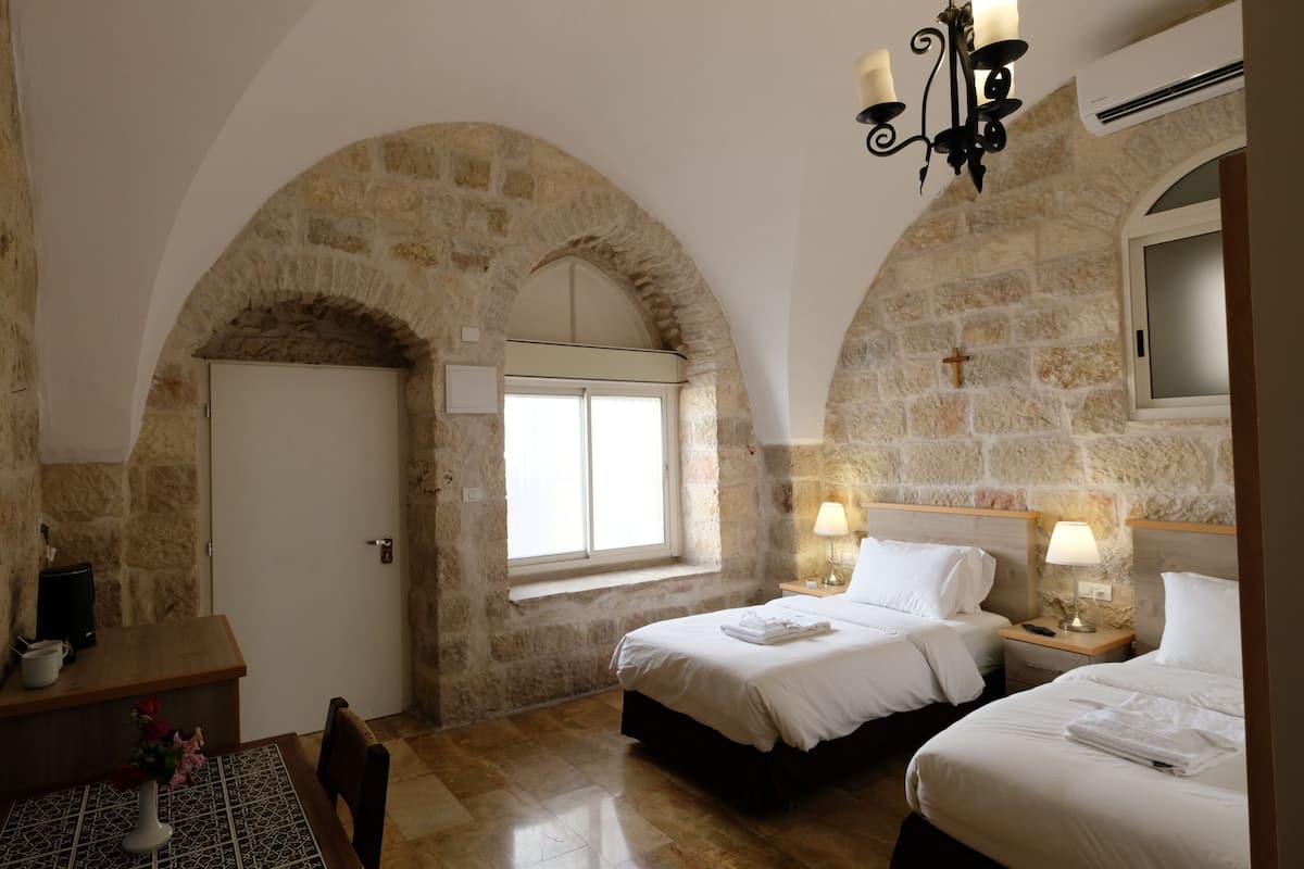 A room with stone walls, a bed, a bedside table, a lamp, and a TV.