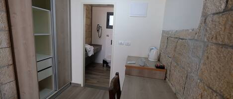 Una habitación compacta con un armario de madera, una pequeña kitchenette y un baño visible a través de una puerta abierta.