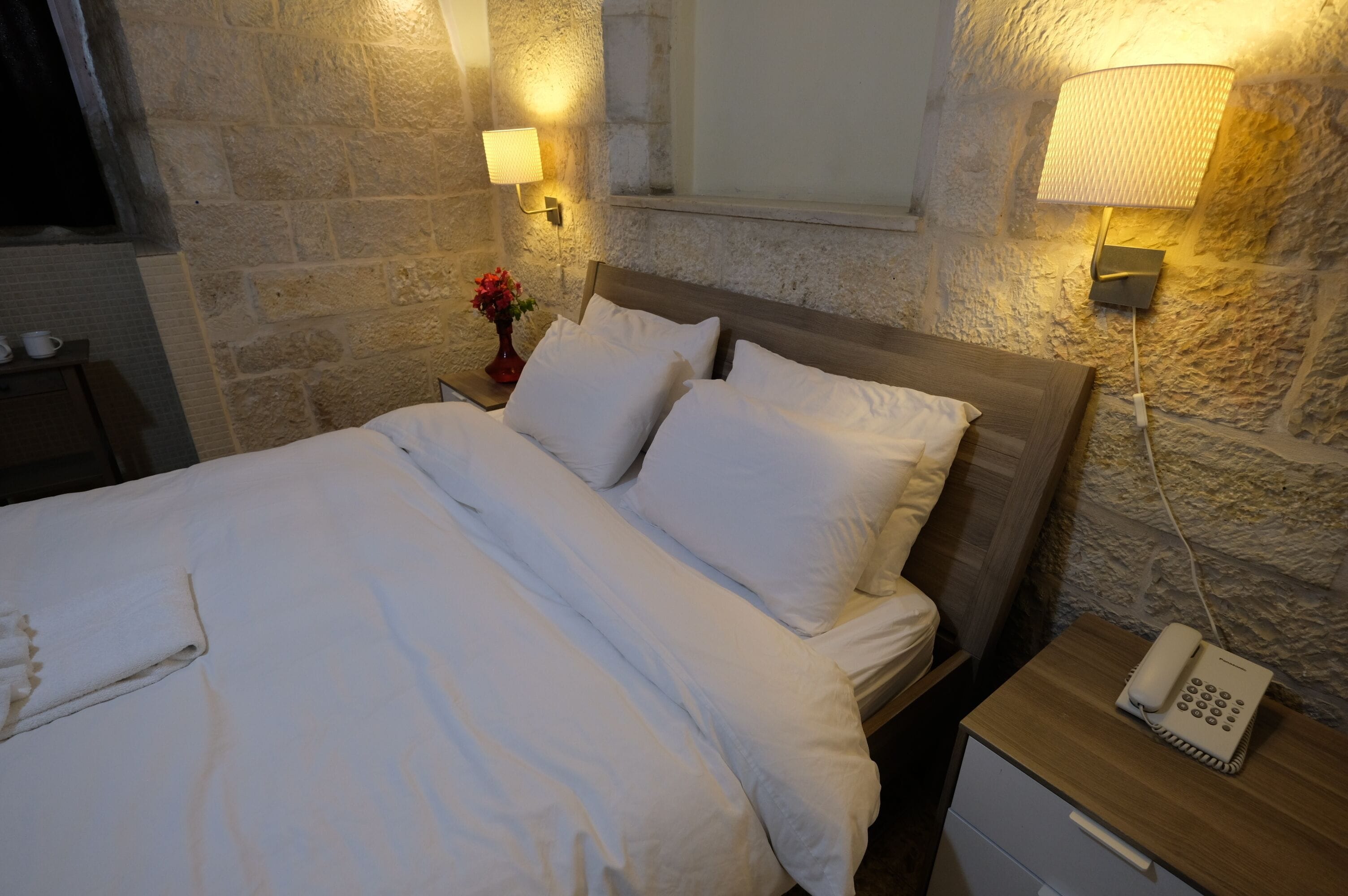 A neatly made bed with white linens, a wooden headboard, and a bedside table with a lamp and a phone.