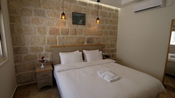 A neatly made bed with white linens, a wooden headboard, and a nightstand with a vase of flowers.