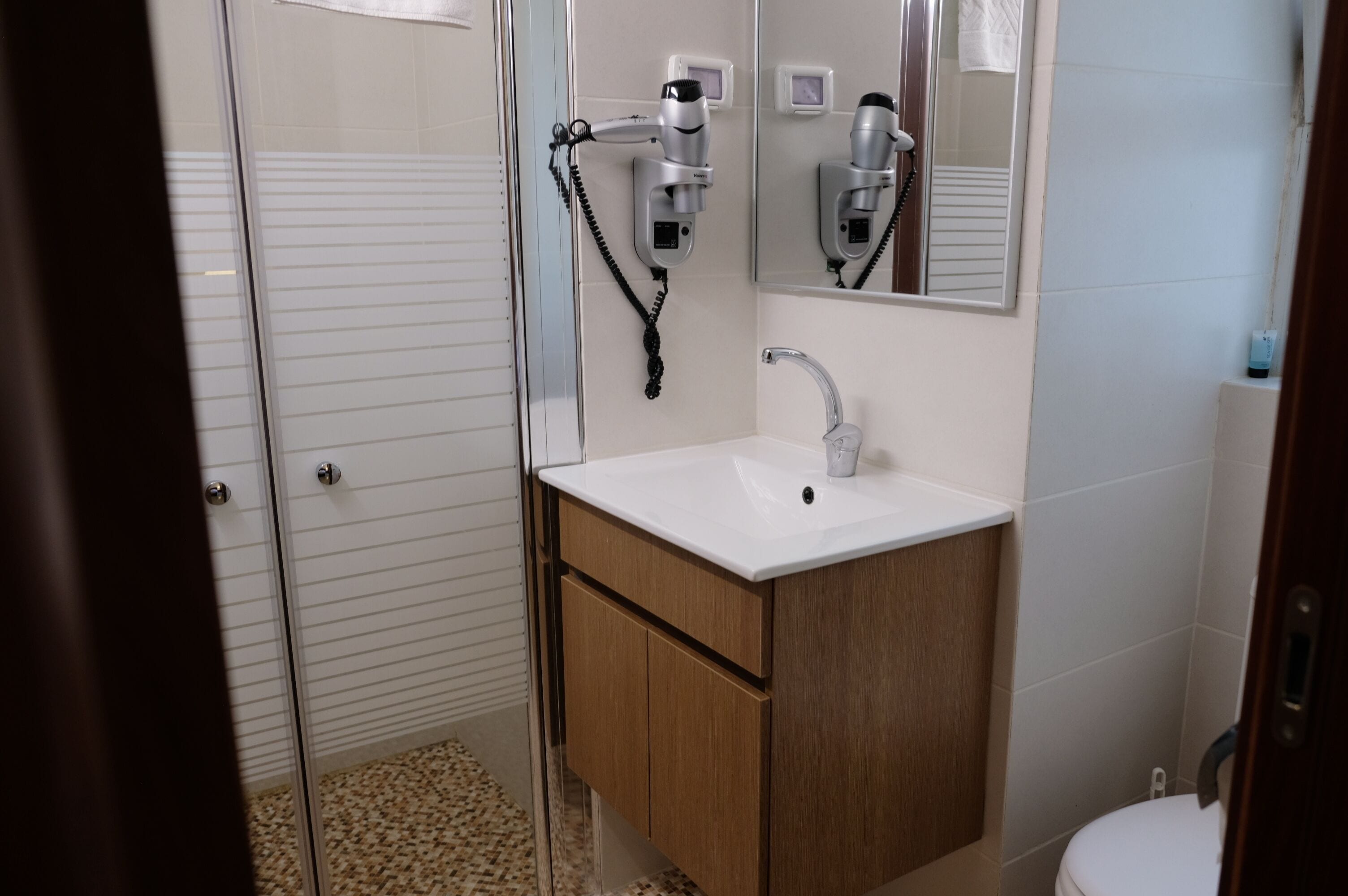 A bathroom with a glass shower enclosure, a white sink, wooden cabinets, and a mirror.