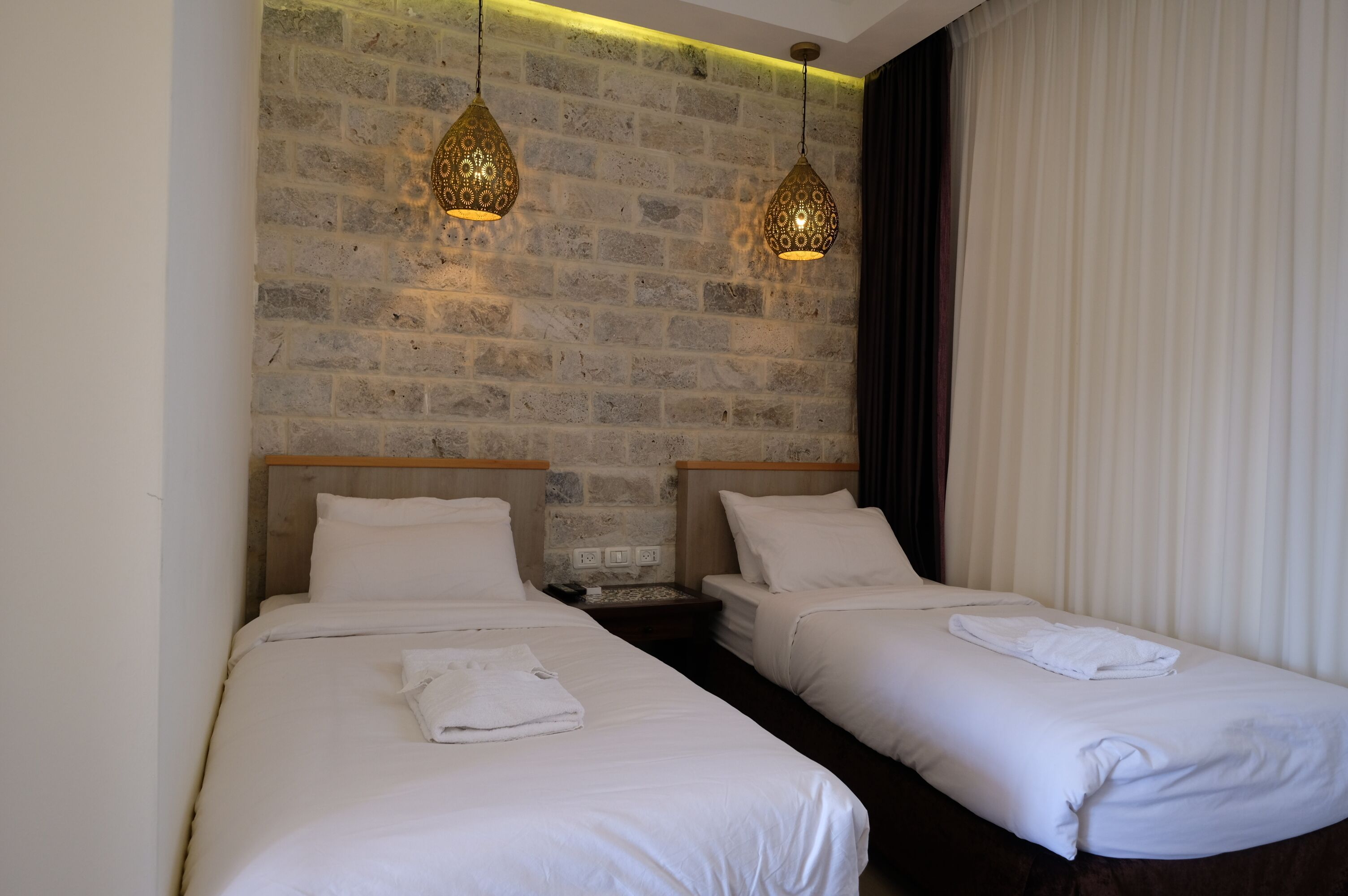 A hotel room with two beds, a brick wall, and hanging pendant lights.