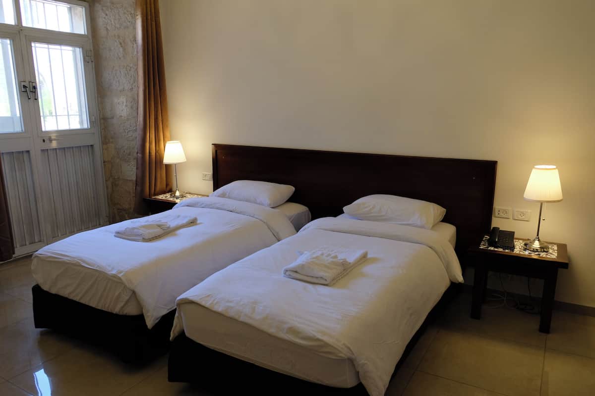 A hotel room with two beds, each with a pillow and a folded towel. There are bedside lamps and a small table with a phone.