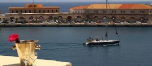 A waterfront view with a boat, a building with arched windows, and a row of parked cars. - Florence (Syros)