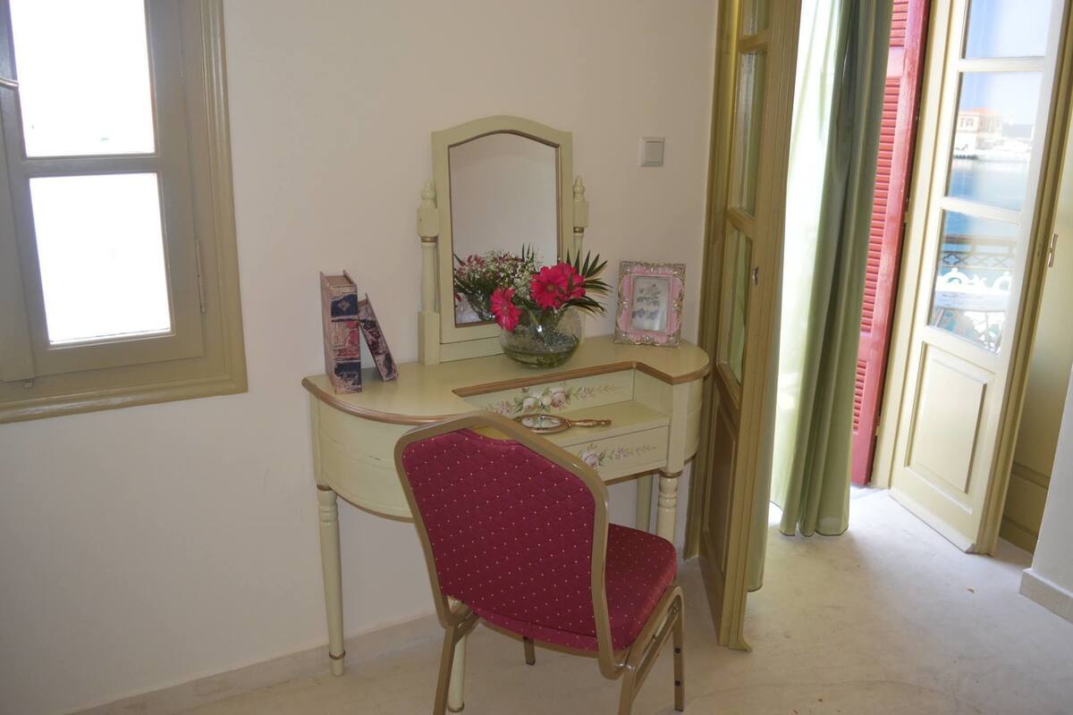 A room with a vanity table, a mirror, a chair, and a window.