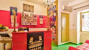 A reception area with a red desk, a chandelier, a wall clock, and a colorful floral mural. - Florence (Syros)
