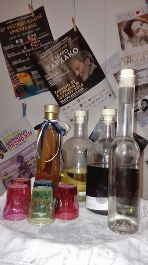 A table with various bottles and colorful glasses, surrounded by posters and flyers. - Florence (Syros)