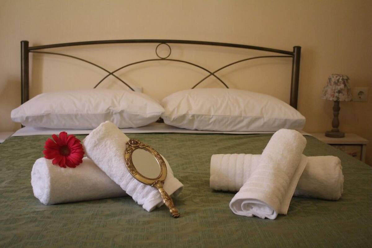 A neatly made bed with white pillows, a green bedspread, and rolled towels.
