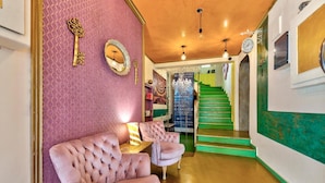 A hallway with a pink upholstered sofa, a decorative key, and a mirror on the wall. - Florence (Syros)