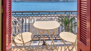 A balcony with two white chairs and a small round table, overlooking a body of water with buildings in the background. - Florence (Syros)