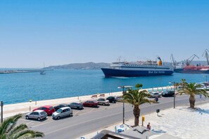 A coastal road with parked cars and a large ferry named "Blue Star Ferries" docked at the port. - Florence (Syros)