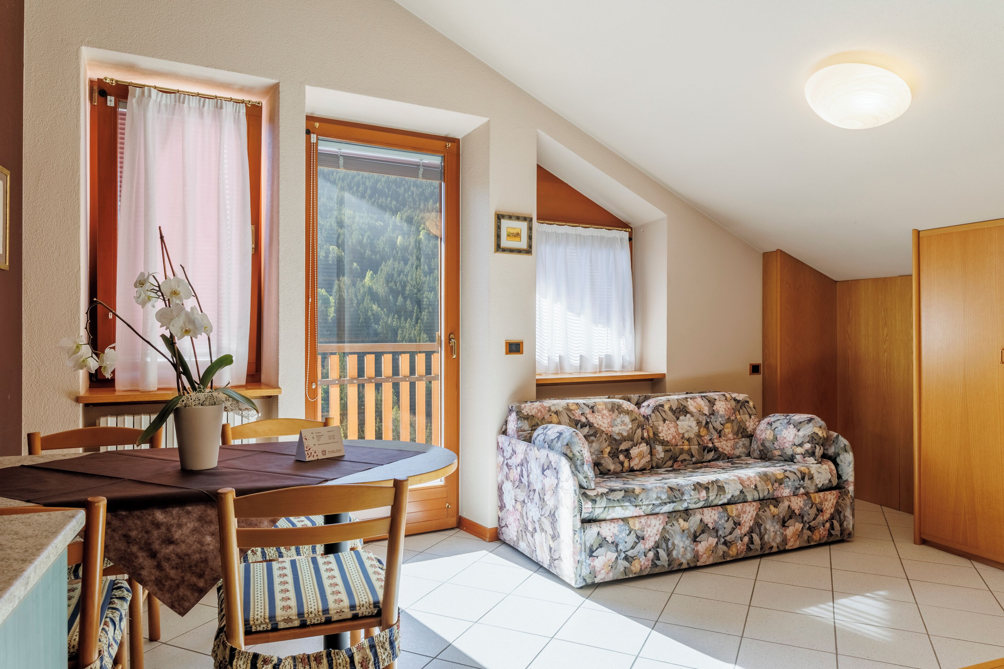 Ein Essbereich mit Tisch und Stühlen, einem floralen Sofa und Blick ins Freie durch ein Fenster.