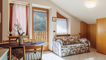 Ein Essbereich mit Tisch und Stühlen, einem floralen Sofa und Blick ins Freie durch ein Fenster.