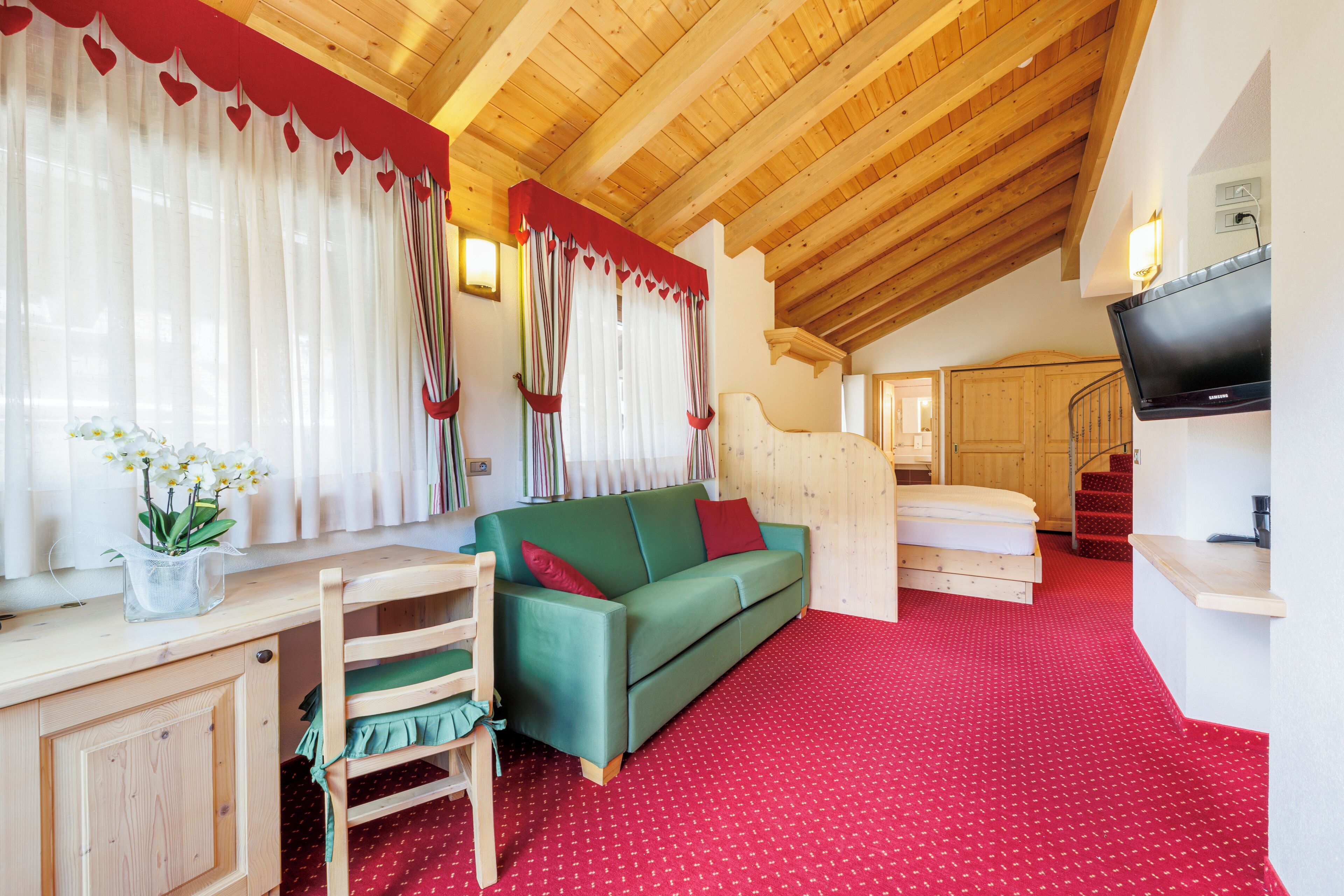Ein gemütliches Zimmer mit einem grünen Sofa, einem Holzstockbett und einem an der Wand befestigten Fernseher.