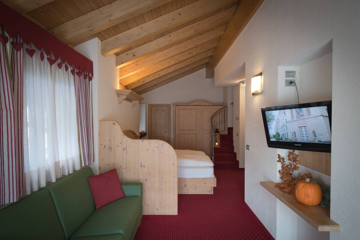 Una habitación acogedora con techo de madera, un sofá verde, una cama, un televisor y una escalera.