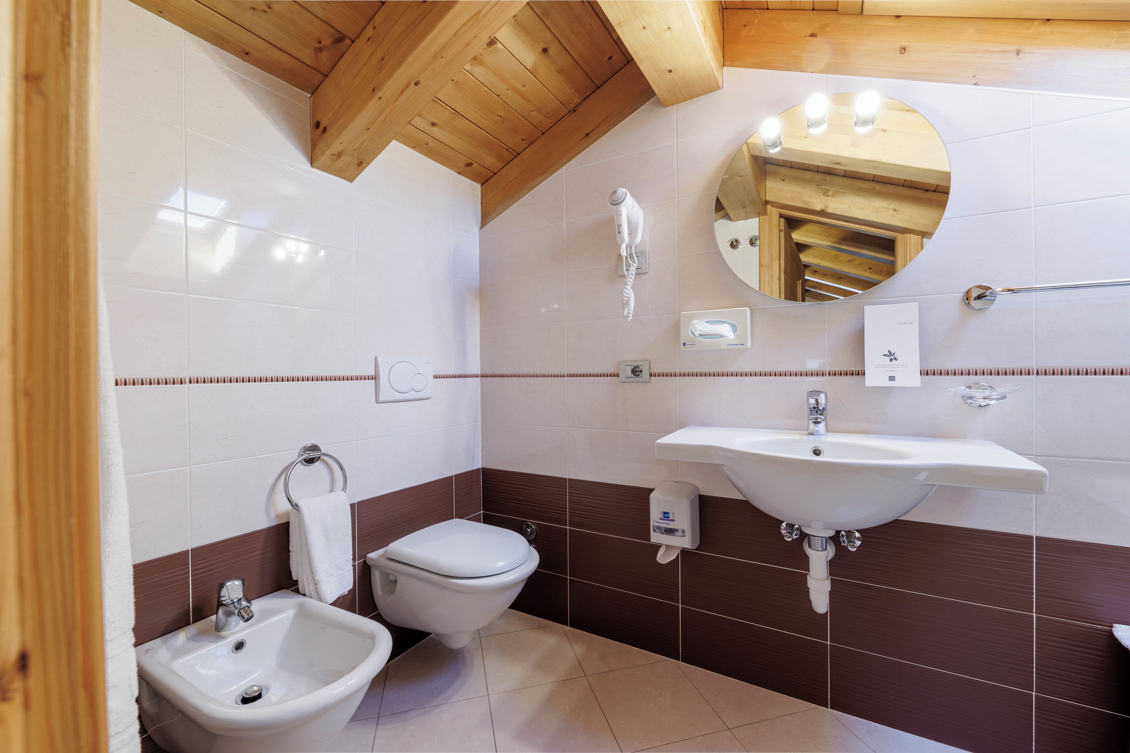 Un baño con techo de madera, un lavamanos blanco, un inodoro y un bidé.