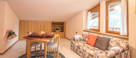 A cozy living room with a round table, floral sofa, and a view of the outdoors through a window.